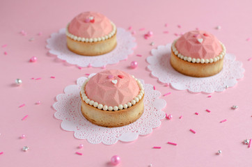 Mousse mini tarts covered with pink velvet spray decorated with sugar balls on pink background