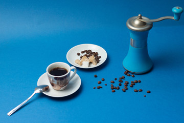 A cup of black coffee with blue coffee grinder on blue background