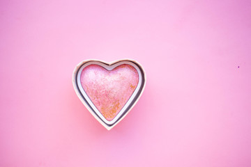 Pink baked highlighter blush in the shape of a heart on a soft pink background