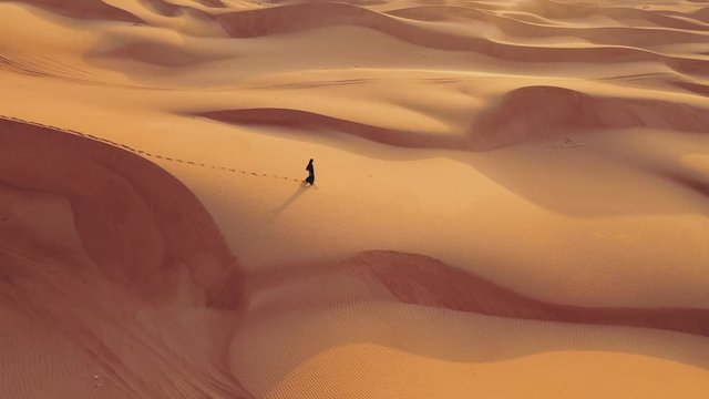 Aerial view from a drone flying next to a woman in abaya United Arab Emirates traditional dress walking on the dunes in the desert of the Empty Quarter. Abu Dhabi, UAE.