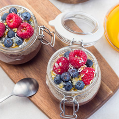Layered chocolate and peanut butter chia seed pudding in a jar, garnished with raspberry, blueberry, honey and coconut flakes, top view, square format