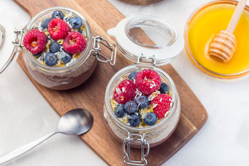 Layered chocolate and peanut butter chia seed pudding in a jar, garnished with raspberry, blueberry, honey and coconut flakes, horizontal, top view
