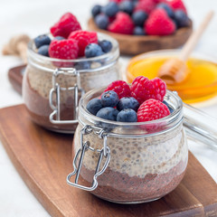 Layered chocolate and peanut butter chia seed pudding in a jar, garnished with raspberry and blueberry, square format