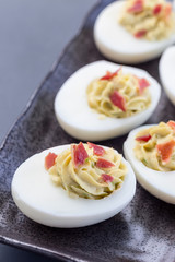 Deviled eggs stuffed with avocado, egg yolk and mayonnaise filling, garnished with bacon, vertical