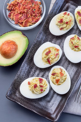 Deviled eggs stuffed with avocado, egg yolk and mayonnaise filling, garnished with bacon, vertical top view