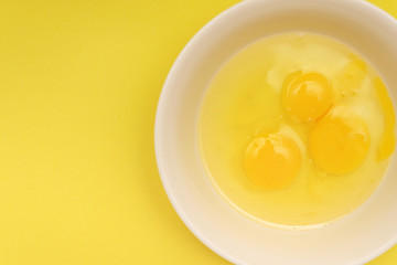 three broken chicken eggs in a plate. fresh raw protein food. yellow background.