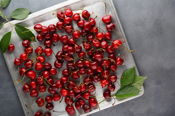 Fresh ripe sweet cherry is scattered on a metal tray on an old table.