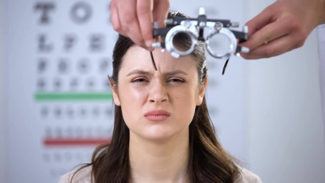 Female squeezing eyes, oculist putting refractor on smiling lady patient, lenses
