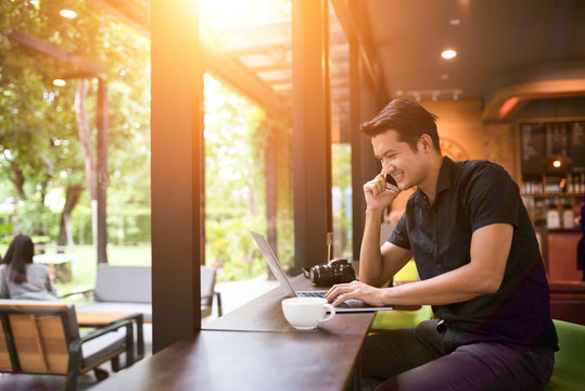 Stylish modern guy talking with a smartphone and using a laptop in a coffee shop