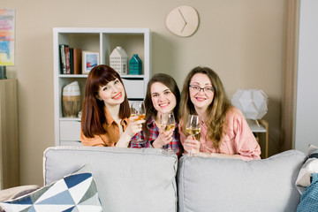 Group of three young pretty women raising their glasses and making a toast with wine. Girls party at home