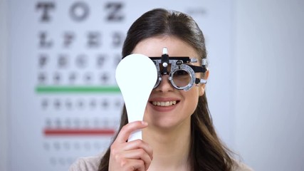 Woman in phoropter closing one eye and smiling, choosing correct lens diopter