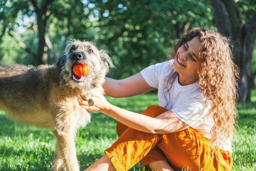 Young happy charming girl playing with her dog with a ball in the park
