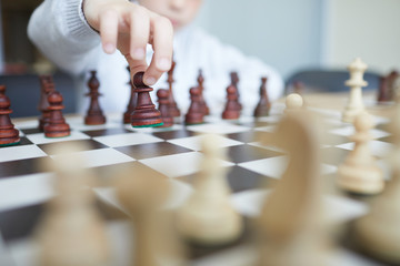 Hand of schoolboy in white shirt making chess move with dark chess piece in response to move of...