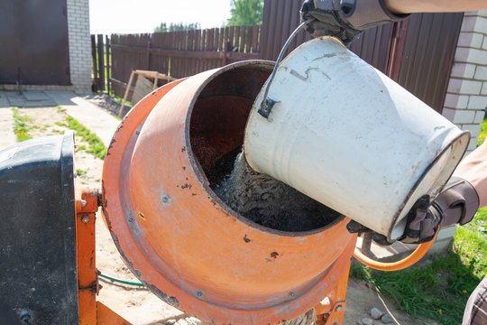 builder working with shovel during concrete cement solution mortar preparation. construction worker with a bucket in his hands loads a concrete mixer.orange concrete mixer prepares cement mortar