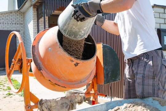 builder working with shovel during concrete cement solution mortar preparation. construction worker with a bucket in his hands loads a concrete mixer.orange concrete mixer prepares cement mortar