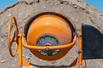 builder working with shovel during concrete cement solution mortar preparation. construction worker with a bucket in his hands loads a concrete mixer.orange concrete mixer prepares cement mortar