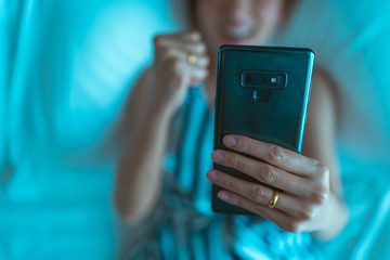 happy woman reading news in smartphone a sitting on a bed in the bed room at home