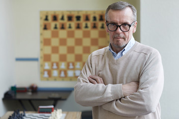 Aged male principal of chess club posing for pictures for advertising chess classes for...