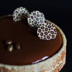 Chocolate coffee mousse cake covered with chocolate glaze and decorated with chocolate elements on black background