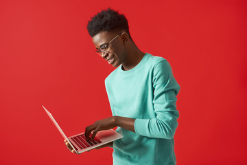 Young African American man standing with laptop and smiling - obrazy, fototapety, plakaty