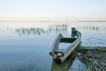 Naklejka premium An old wooden boat on the sandy shore of a large lake. Sunrise on Svityaz Lake. Ukrainian nature. Copy space.