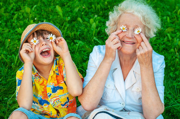 Happy grandmother and grandchild fooling around the lawn of putting chamomiles instead of eyes....