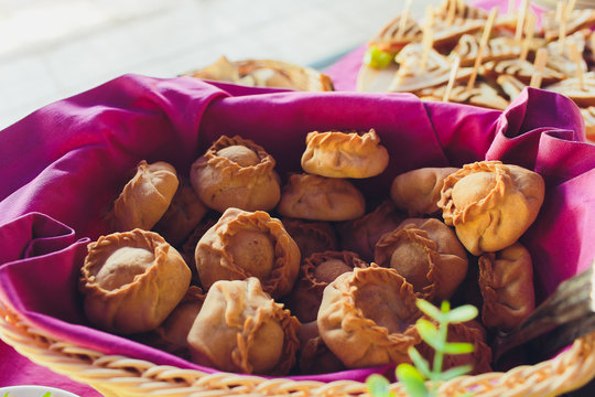 Homemade baked uchpuchmak samsa with meat and potato on a wooden plate.