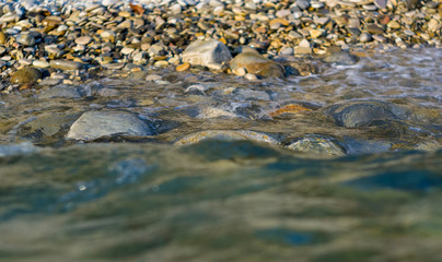 pebble stones on the sea beach, the rolling waves of the sea with foam