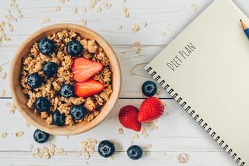 Homemade granola and fresh berries on wood table with note book and text diet plan concept, copy space.