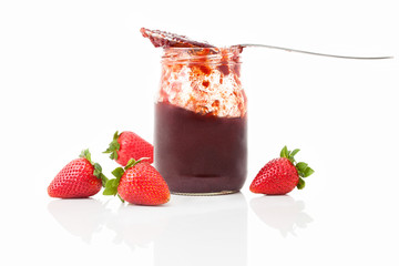 Strawberry preserve with spoon and fresh fruits around on the back, isolated on white background with shadow reflection. On the glass is laid spoon