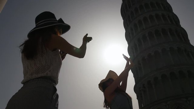 A woman holds the tower of Pisa for a photo and another photographs her. Italy - Pisa.