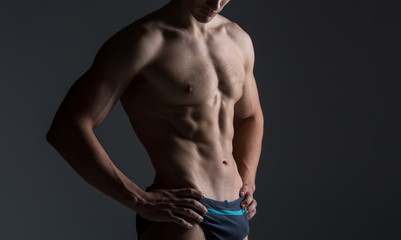 Young male athlete bodybuilder posing. Handsome athletic male power guy. Fitness muscular person. Young athlete showing muscles in the studio. six packs muscles posing shirtless on gray background