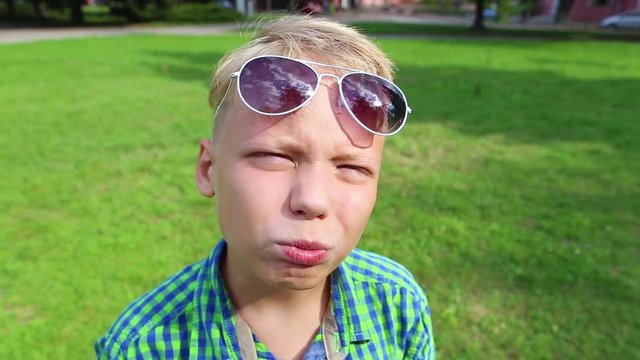 Closeup portrait of cute funny little white kid posing before camera wearing sunglasses. 10 years old boy looiking at camera and making different silly faces cheerfully.