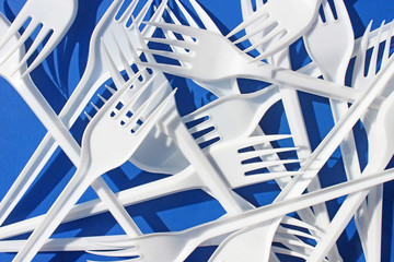 A lot of white plastic forks close-up on a blue background.