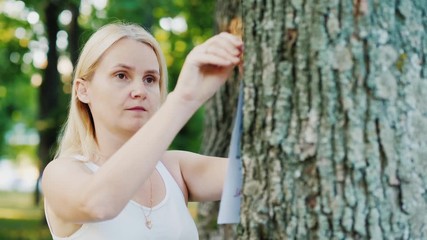 Young woman attaches an ad to a tree in the park