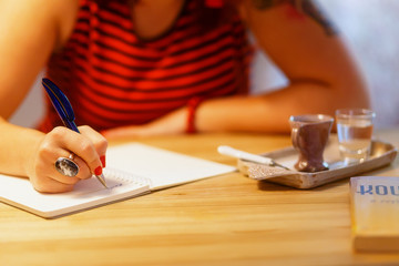 Close up of lady's hand writing in notepad in coofee bar.