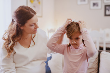Caring beautiful pregnant mother making new hairstyle to her cute daughter.