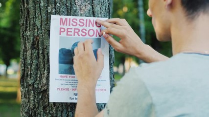 A young man puts up ads for a missing person in the park