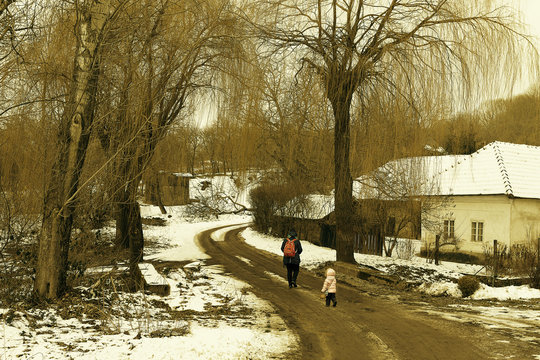 Ramble trough old village, sepia effect photography. Walking in old dorp in winter. Mother and doughter walking-up on the road under tall goat willows. Romantic ramble in old ham. Child in settlement