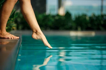 Fotobehang Closeup young female leg touch blue water in swimming pool © Kate