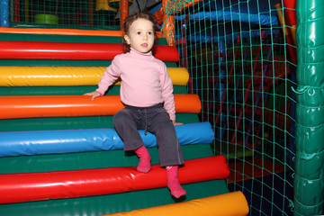 Fototapeta na wymiar little cute curly baby girl playing in a children's entertainment center in the game maze. The child plays in the playground