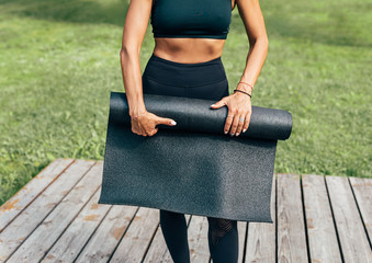 Unrecognizable fit woman rolling exercise mat outdoors
