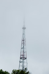 Obraz premium high television tower stands on the background of the cloudy sky. metal tower spire in the fog. concept sinister background