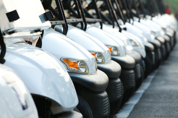 Golf cars or golf carts in a row outdoors on a sunny spring day