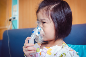 Sad asian child holds a mask vapor inhaler for treatment of asthma. Breathing through a steam...