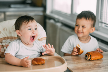 charming children in the kitchen during the day eating buns with poppy seeds, boy and girl