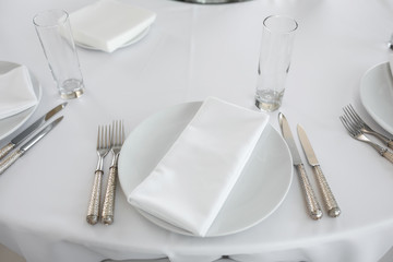 Wedding table setting decorated with fresh flowers. White plates, silverware, white tablecloth and white room. Wedding floristry. Banquet table for guests. Bouquet with roses, hydrangea and eustoma