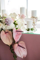 The wedding table setting for the newlyweds is decorated with fresh flowers of carnation, rose, anthurium and eucalyptus leaves. Silver candlesticks, white candles. Wedding floristry. Close-up details