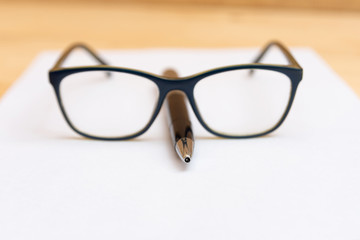 Eyeglasses lie on the handle in the shape of a nose, on a clean and white sheet of paper.