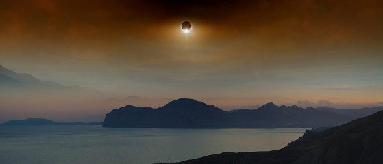 Total solar eclipse in dark red sky above sea and mountains